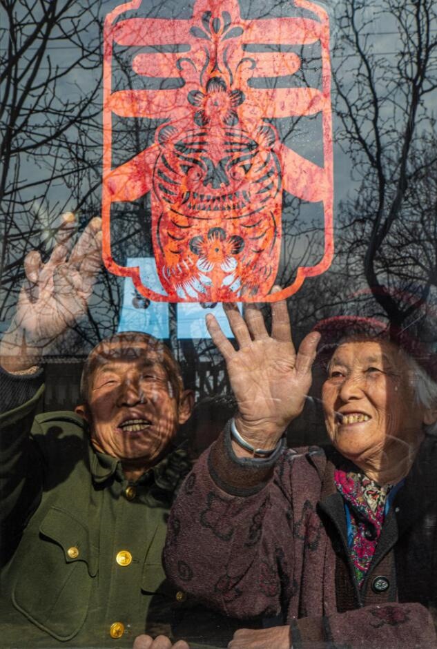 臘月里，霍州市師莊鄉(xiāng)馮南垣村村民師榮光(左)在災(zāi)后重建的新家里貼窗花。(霍州市委宣傳部供圖)