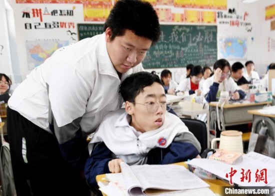 朱金祥(左)把鐘華強(qiáng)放到課堂座位上后，都要把他擺正好，確認(rèn)安全后才回到自己的座位上。 卓忠偉 攝