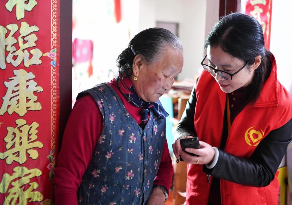 在福州市長樂區(qū)航城街道籌岐村，智慧養(yǎng)老平臺派駐社區(qū)的助老員（右）在為老人陳鳳英（左）講解養(yǎng)老定制手機(jī)的用法（2021年11月26日攝）。新華社記者 魏培全 攝