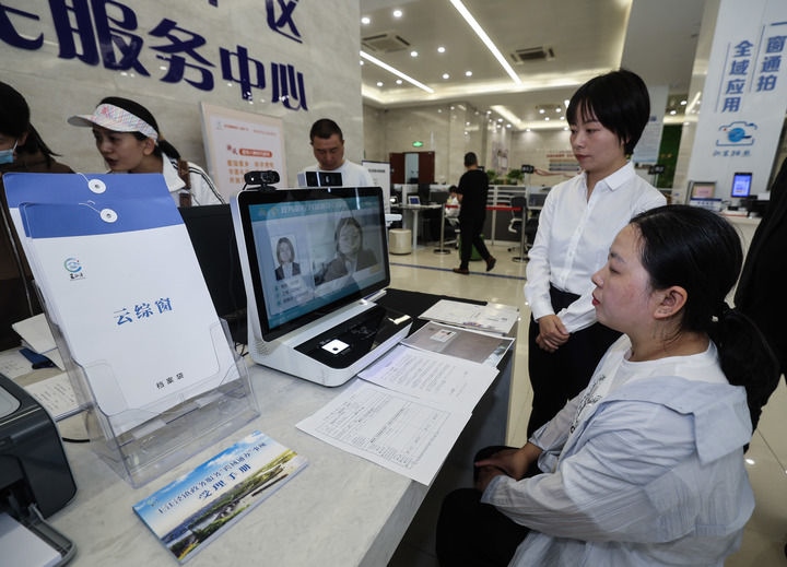 在浙江省嘉興市秀洲區(qū)王江涇鎮(zhèn)便民服務中心的“跨域通辦·云綜窗”窗口，辦理開業(yè)登記的個體工商戶（右一）通過該系統(tǒng)與江蘇省蘇州市吳江區(qū)盛澤鎮(zhèn)行政審批局工作人員視頻連線，進行身份讀取及材料線上審核（2024年5月9日攝）。新華社記者 徐昱 攝