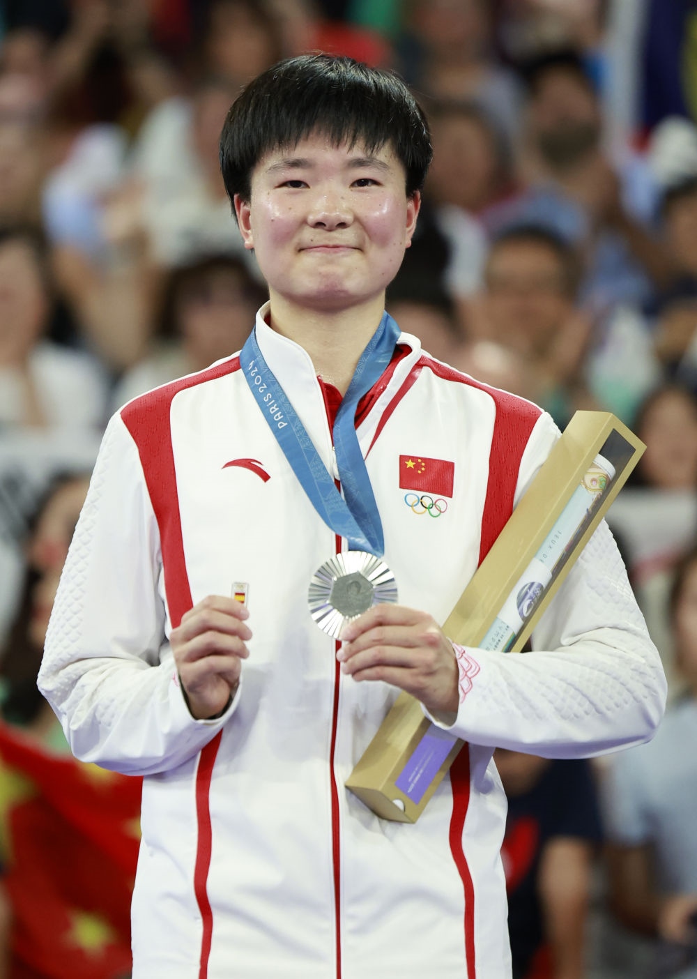巴黎奧運(yùn)會羽毛球女子單打亞軍、中國選手何冰嬌在頒獎儀式上一手握著銀牌，一手握著西班牙奧委會徽章（2024年8月5日攝）。新華社記者 任正來 攝