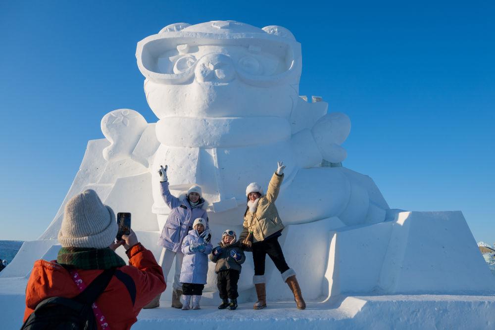 2025年1月3日，在黑龍江哈爾濱冰雪大世界園區(qū)，游客與亞冬會吉祥物雪雕“濱濱”合影